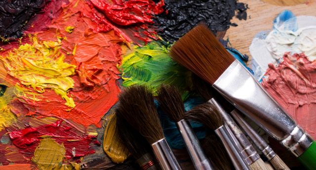 A collection of paint brushes laid out on top of a canvas covered in paint swatches